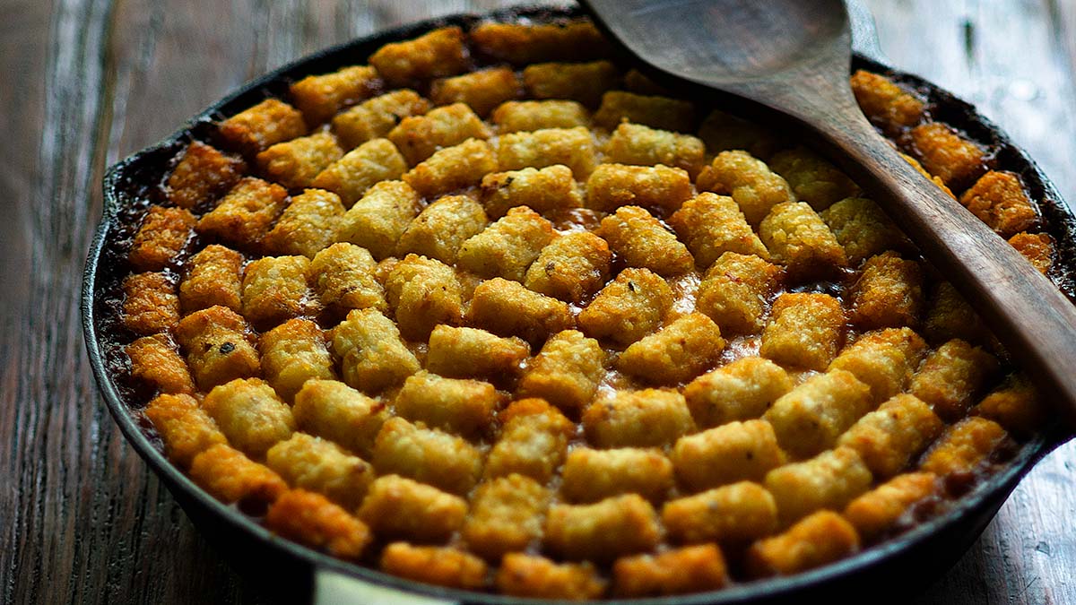 Mexican Style Taco Tater Tot Casserole served family style in a cast iron skillet with a rustic wooden spoon on top.