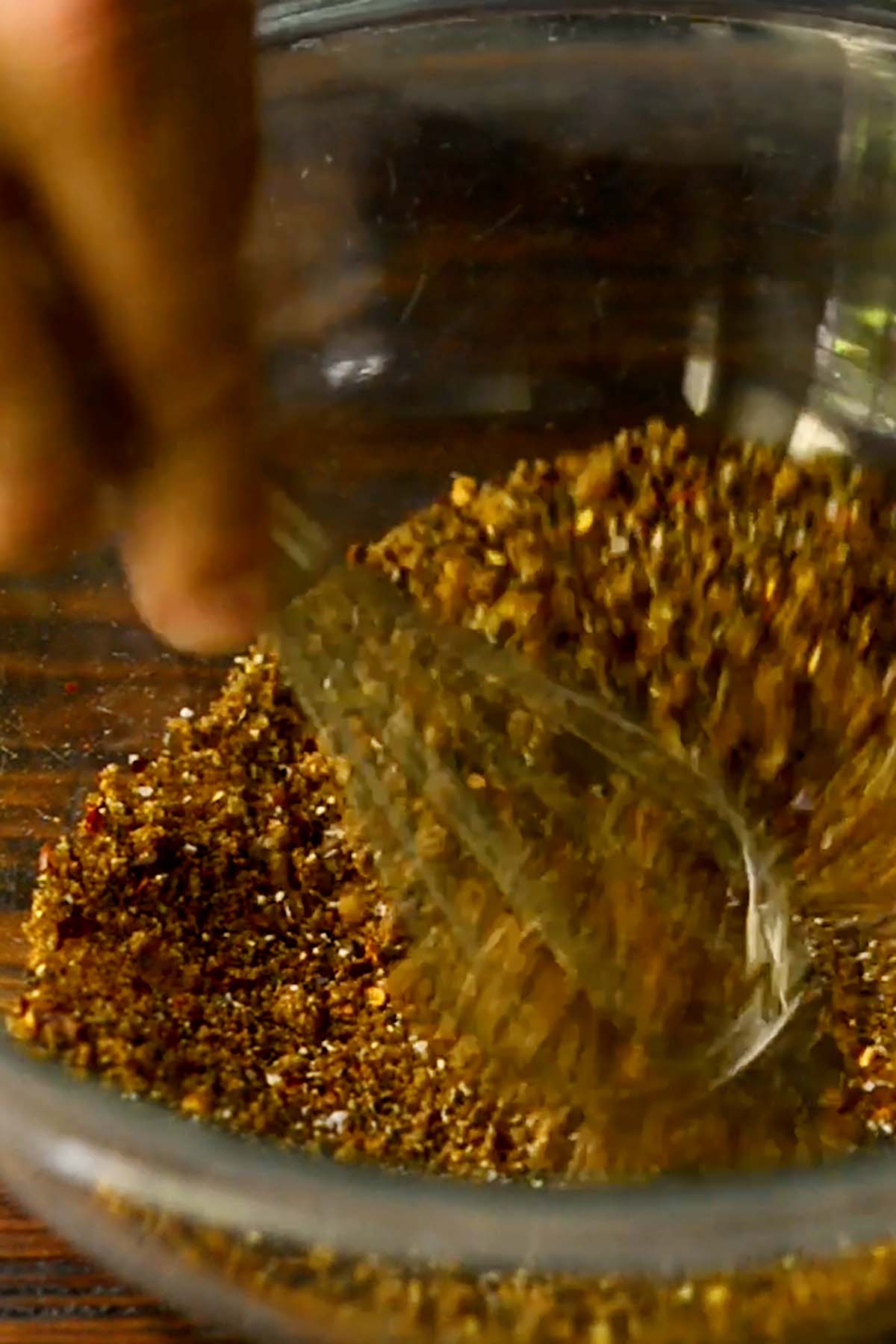 Herbs and spices being whisked in a glass mixing bowl.