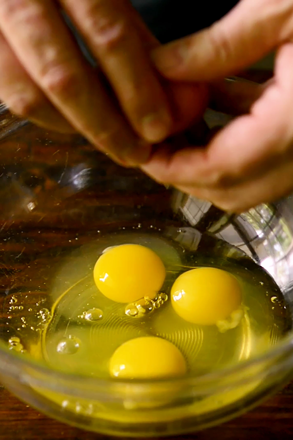 Eggs being cracked into a glass mixing bowl.