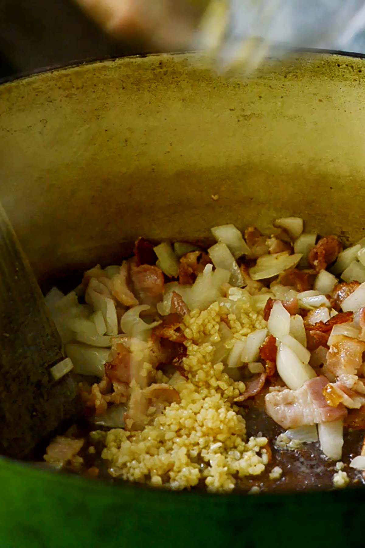 Minced garlic, bacon pieces, and diced onion sautéing in a dutch oven.