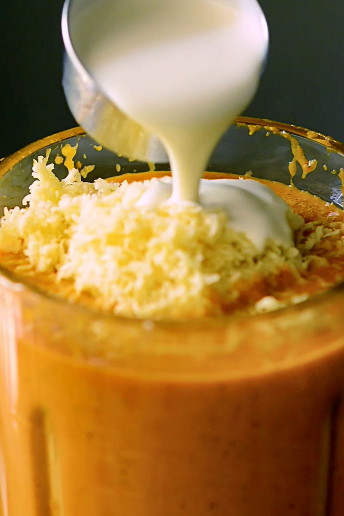 Grated smoked gouda cheese and heavy cream being added to Roasted Bell Pepper soup in a cooking blender.