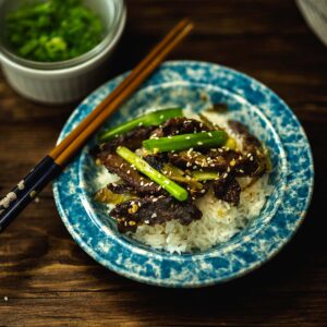 Green Chile Beef Stir Fry served over rice with green onion and topped with roasted sesame oil and sesame seeds.