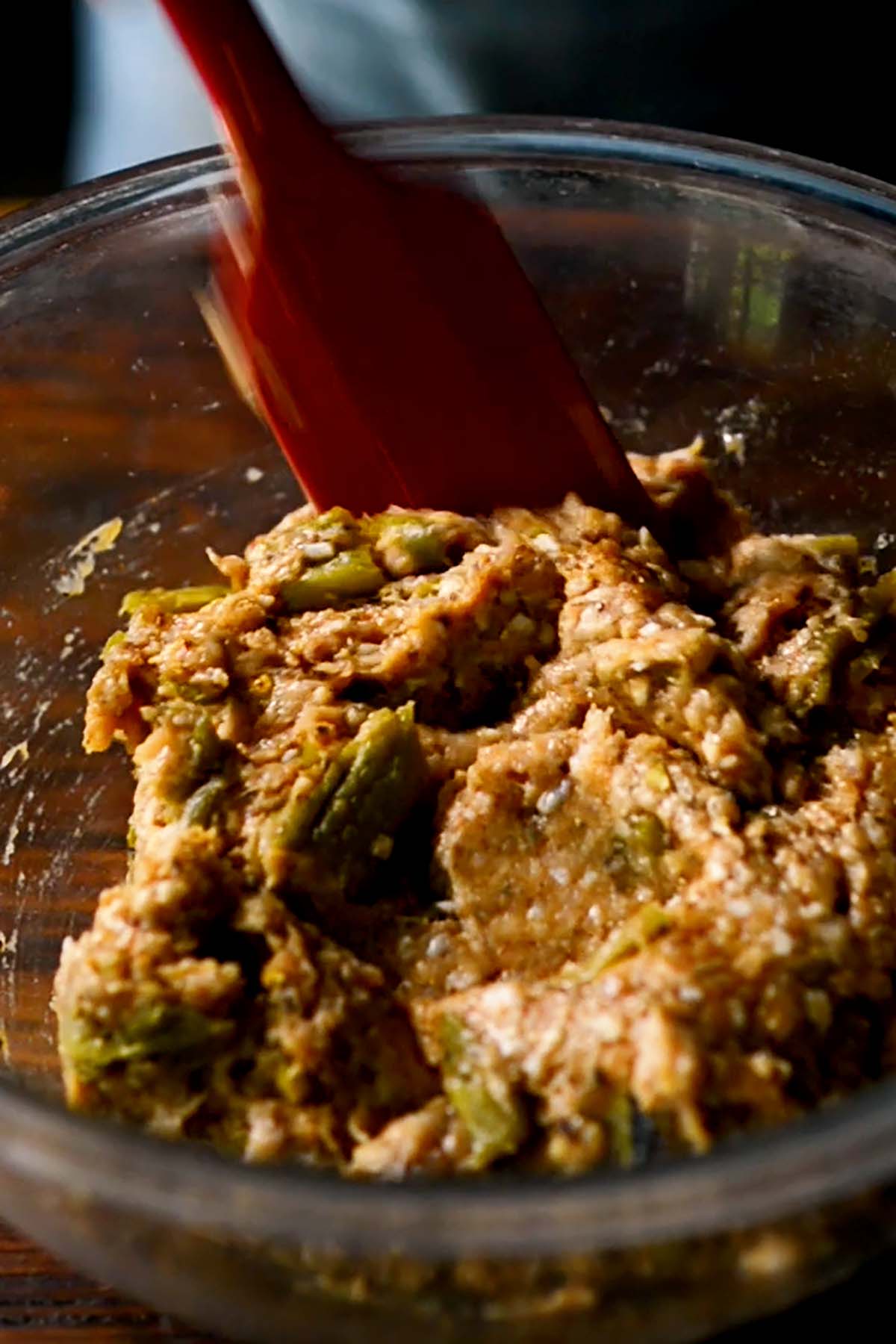 Ground chicken being stirred together with fresh hatch green chiles and a seasoning mix in a glass mixing bowl.