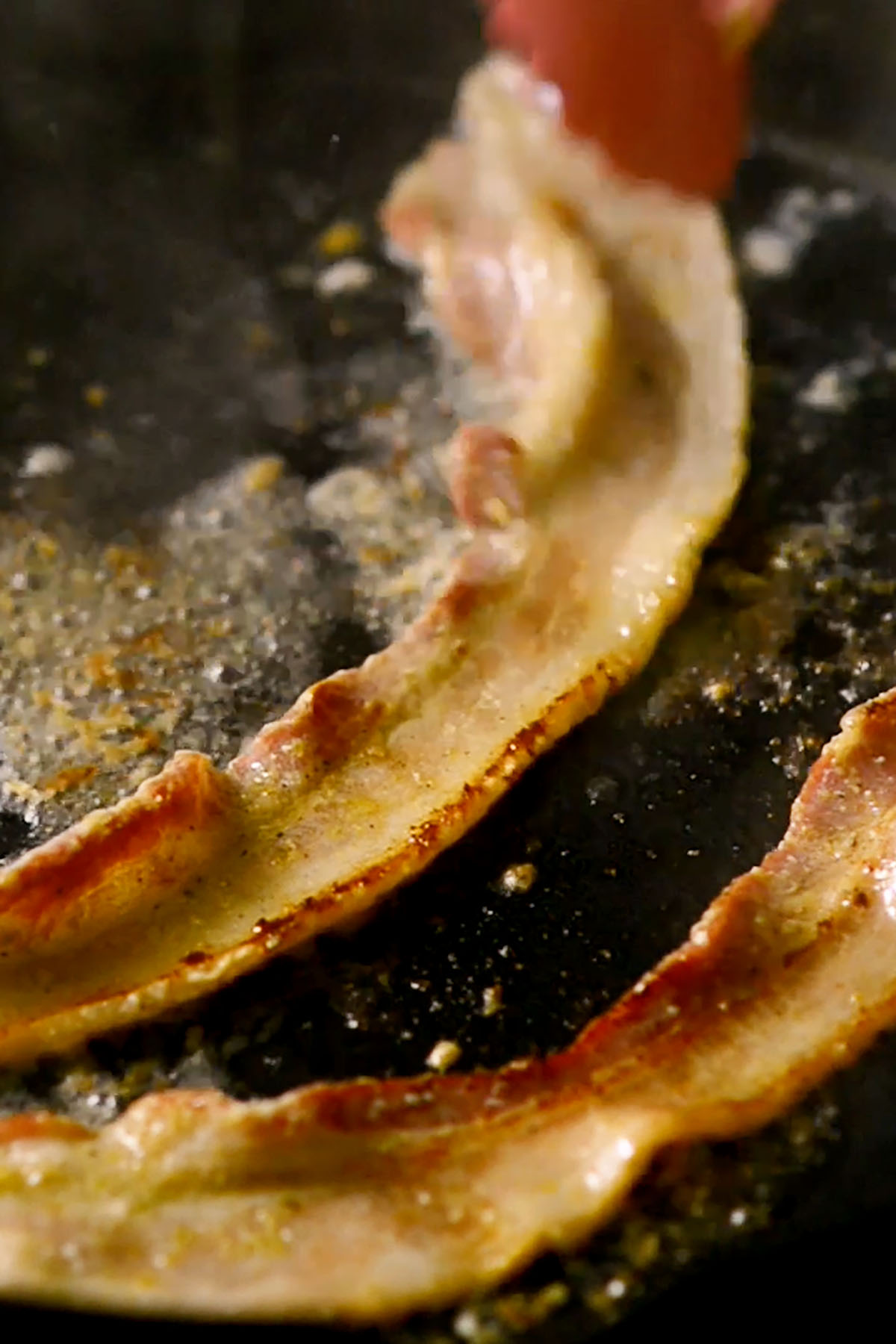 Hatch Green Chile bacon cooking in a cast iron skillet.