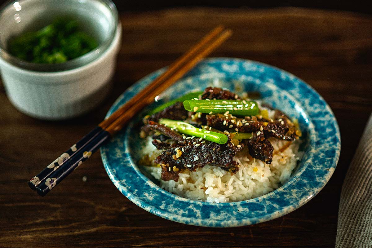 Green Chile Beef Stir Fry served over rice with green onion and topped with roasted sesame oil and sesame seeds.