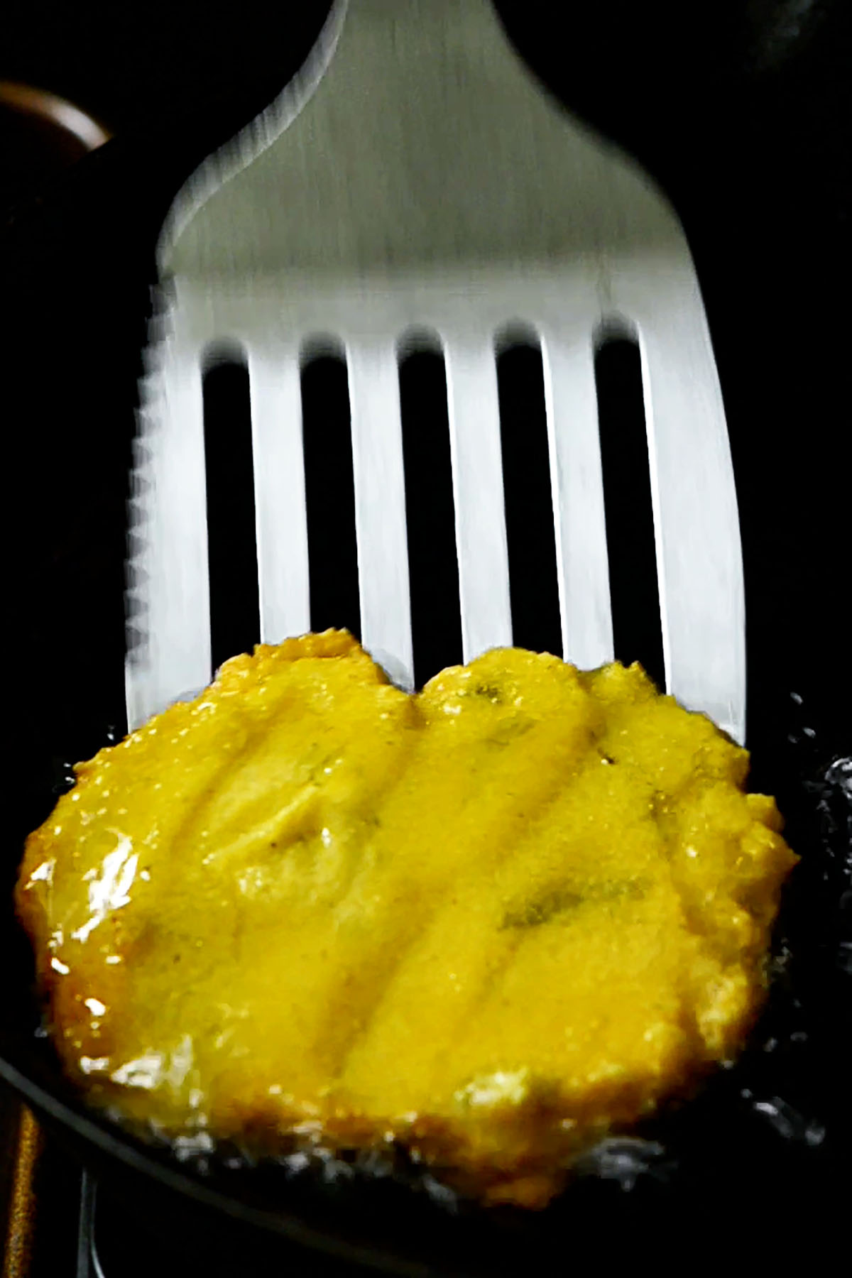 A hot water cornbread patty being flipped in a frying pan.