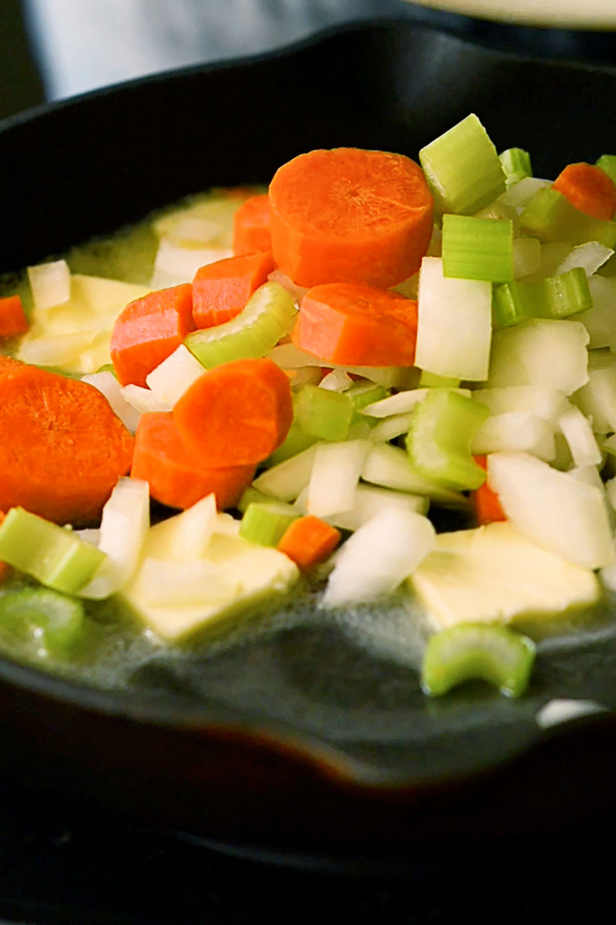 Mixed vegetables and butter cooking in a cast iron skillet.