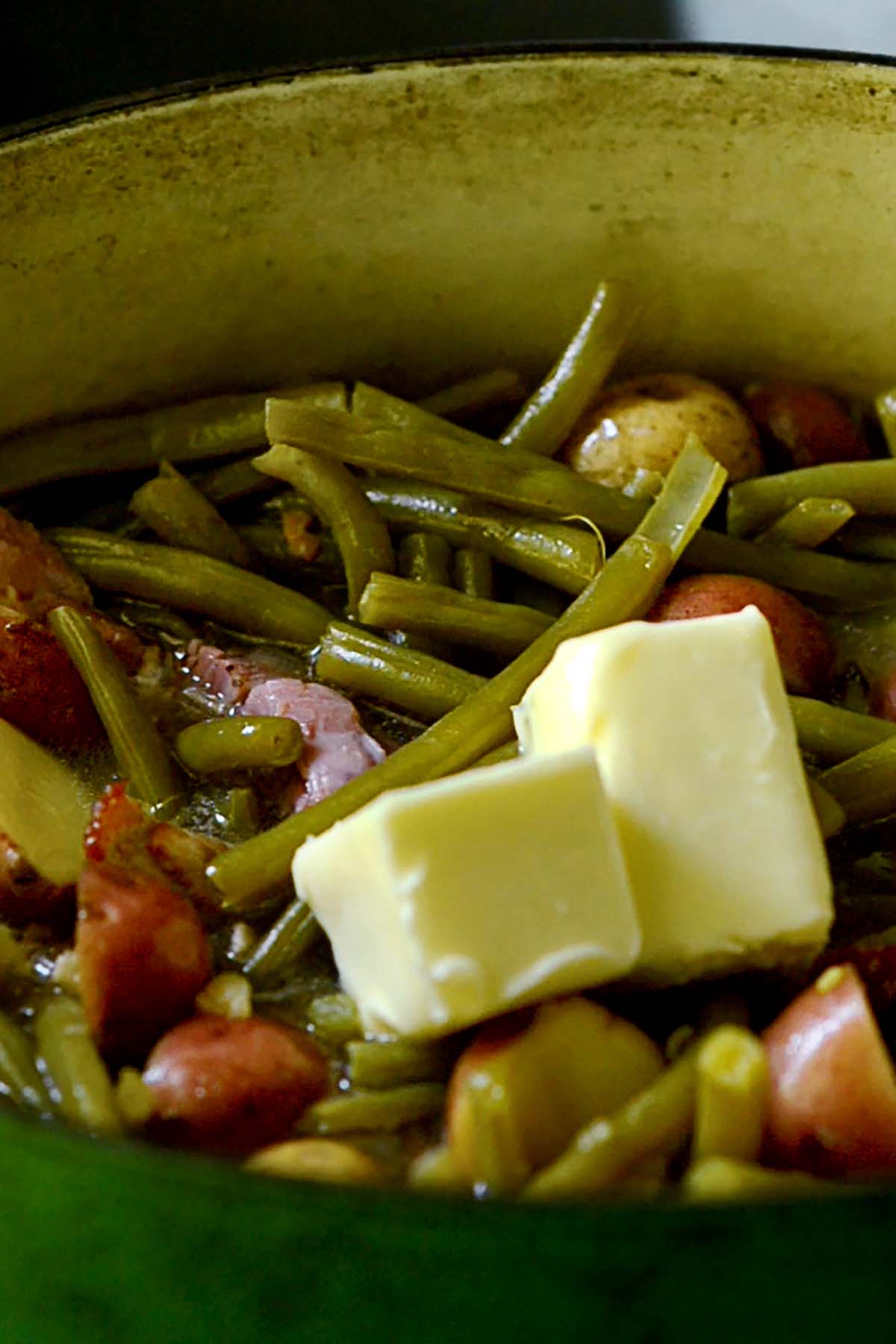 Butter sitting on top of green beans and potatoes before melting in.