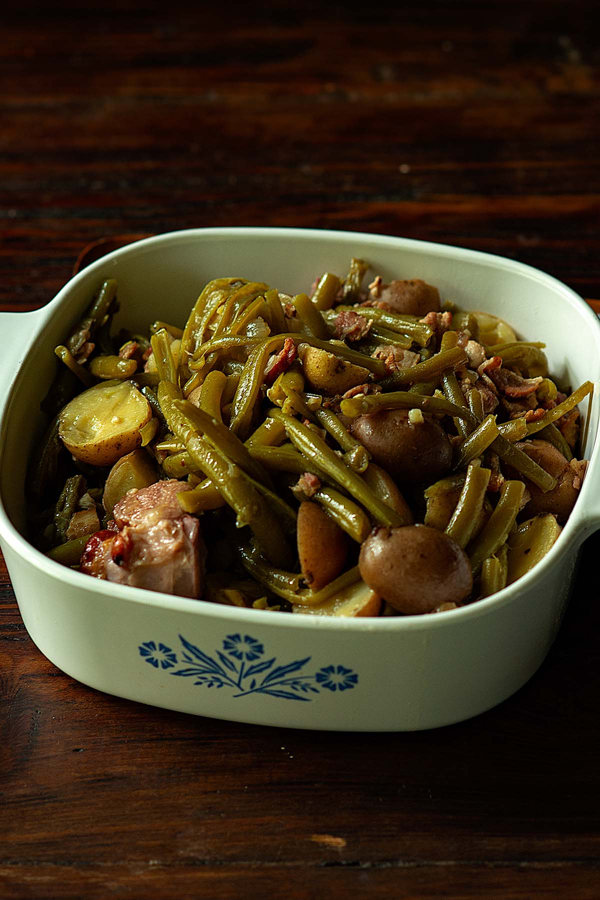 Green beans and potatoes served in a vintage serving dish on a wooden table.