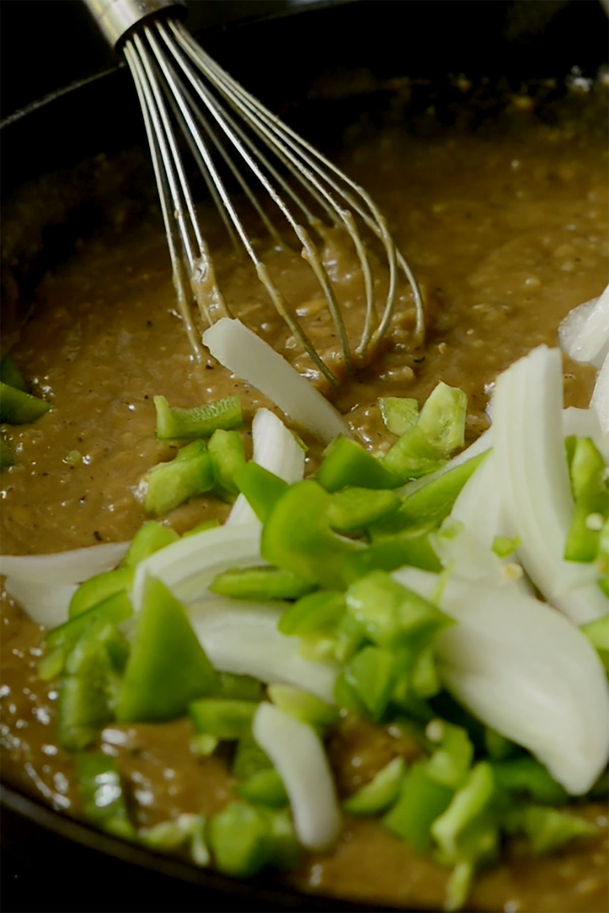 Green bell pepper and onions being stirred into a smother oxtail roux.