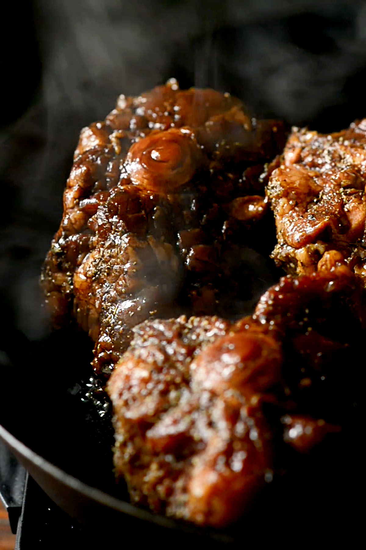 Oxtails searing in a cast iron skillet.