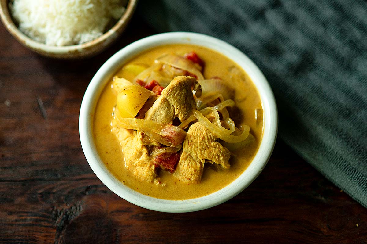 Thai Yellow Curry served in a white bowl with chicken, onion, and potato, piled high in the center of the bowl.