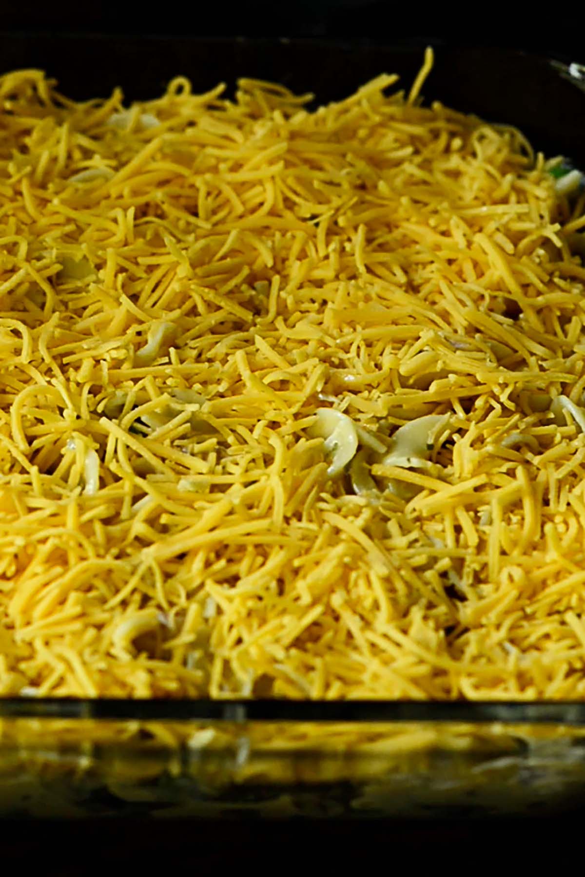 Shredded cheddar cheese evenly spread across the top of unbaked Tuna Noodle Casserole.