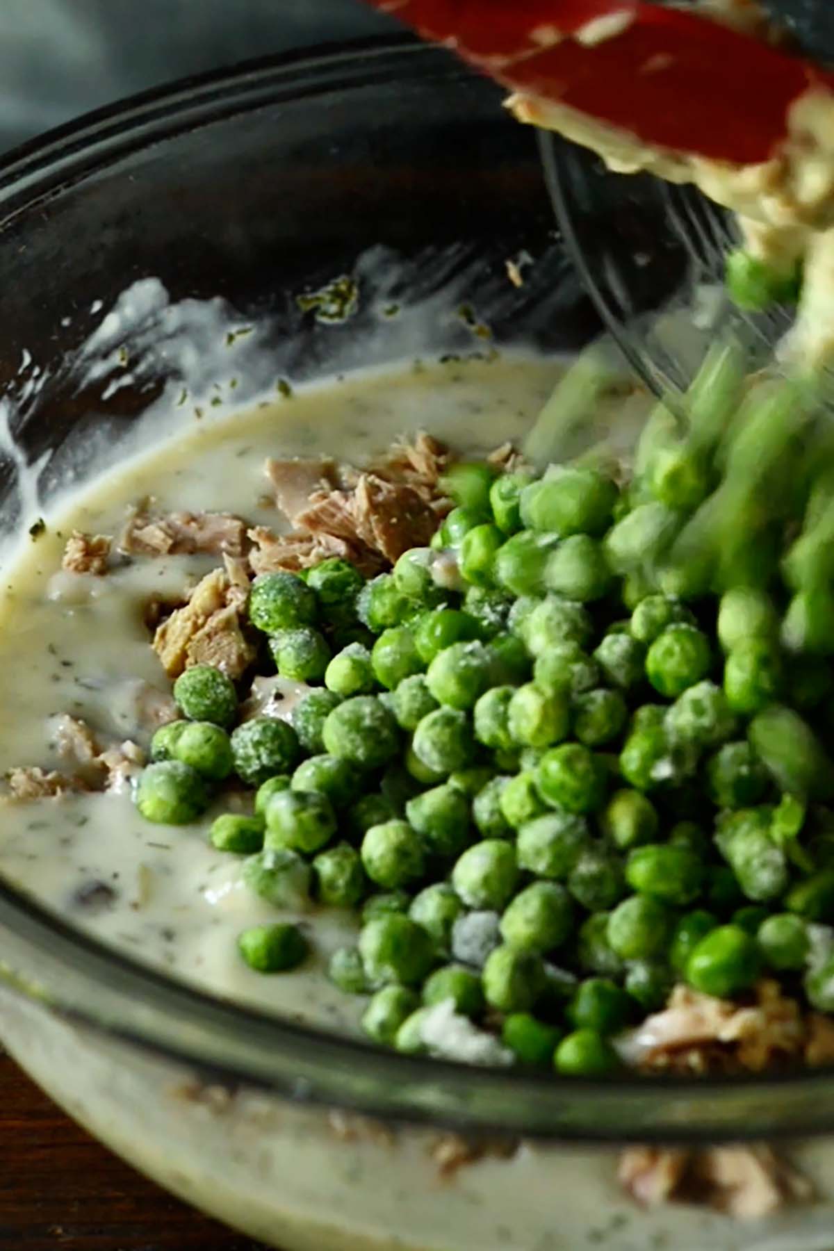 Peas and and canned tuna being added to a bowl of creamy soup mixture for tuna noodle casserole.