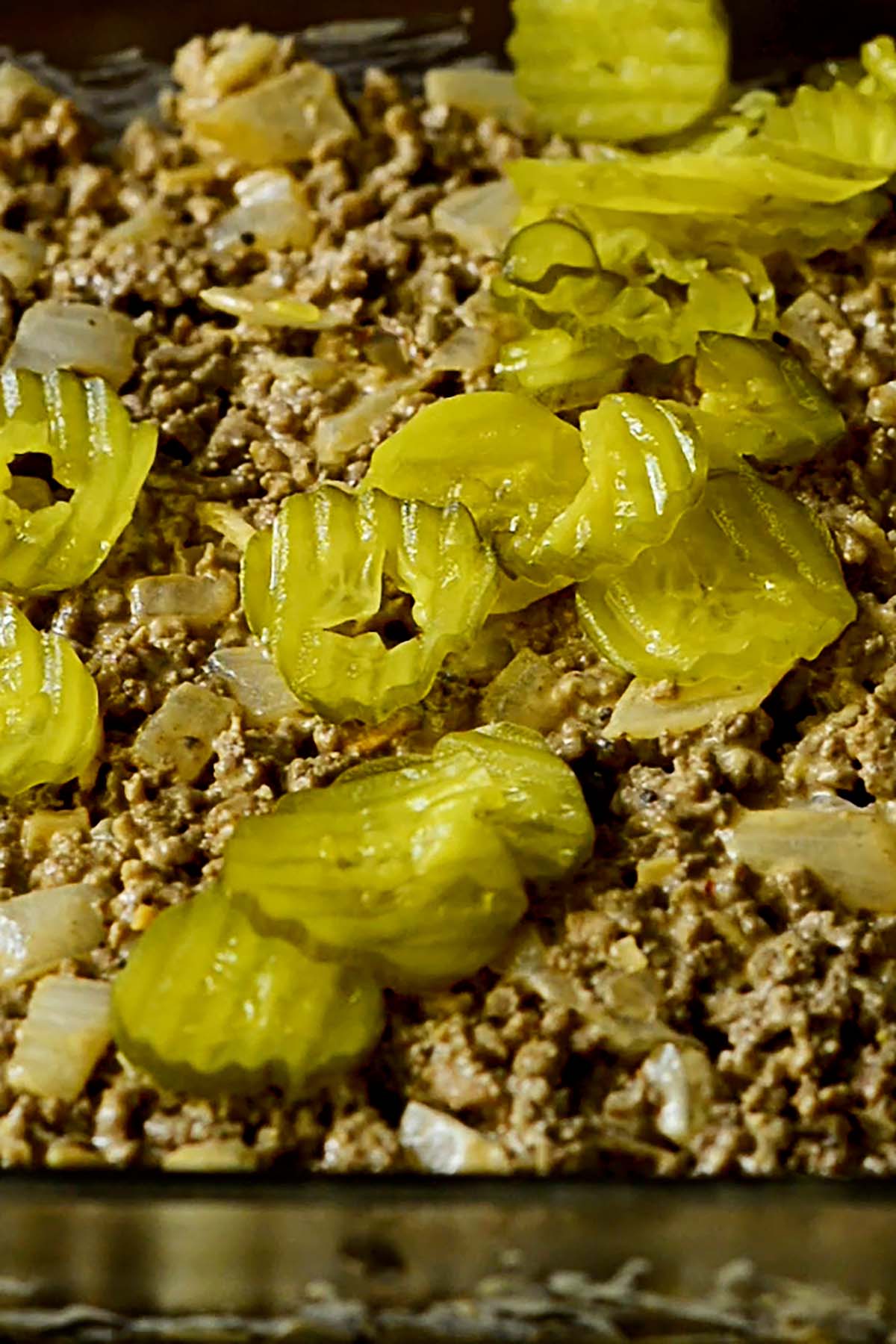 Pickles laid out over the top of a big mac ground beef mixture evenly spread in casserole dish.