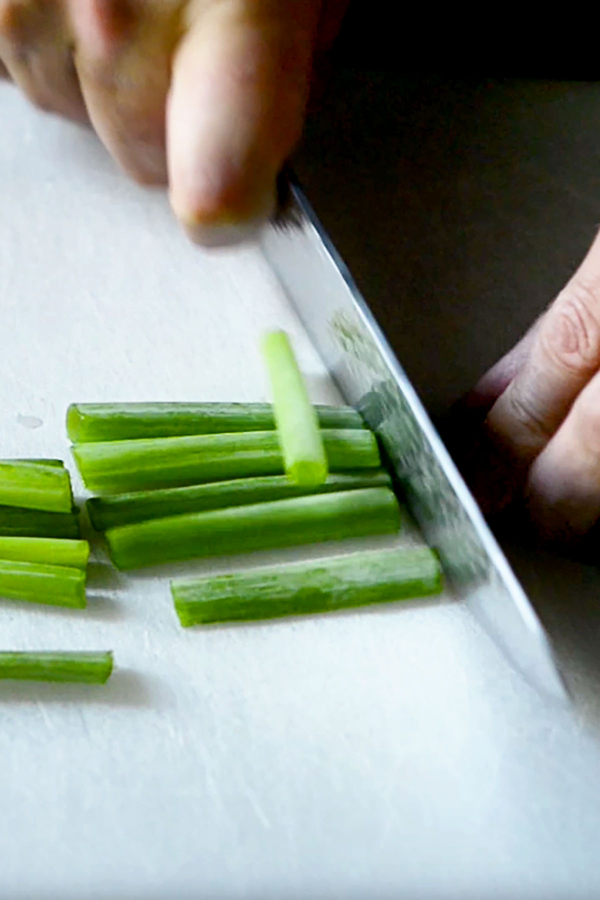 Green onions being sliced into large pieces on a cutting board.