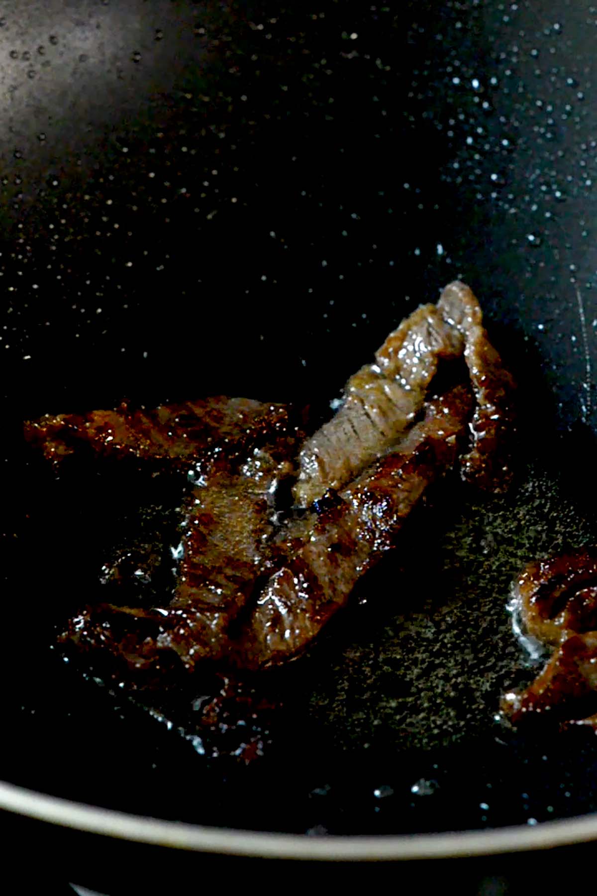 Strips of top sirloin being fried in a wok.