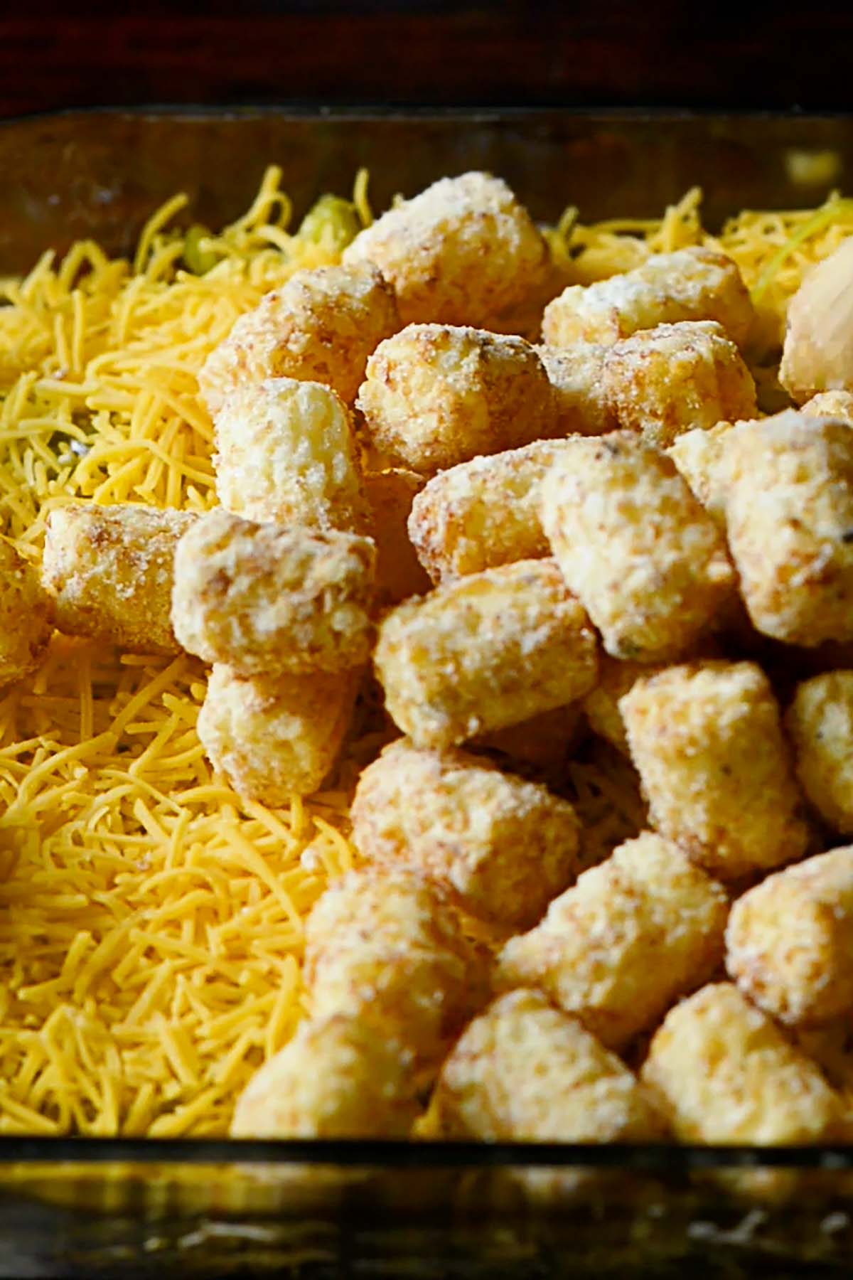 Shredded cheddar cheese and frozen tater tots spread over the top of a Big Mac Casserole with Tater Tots.