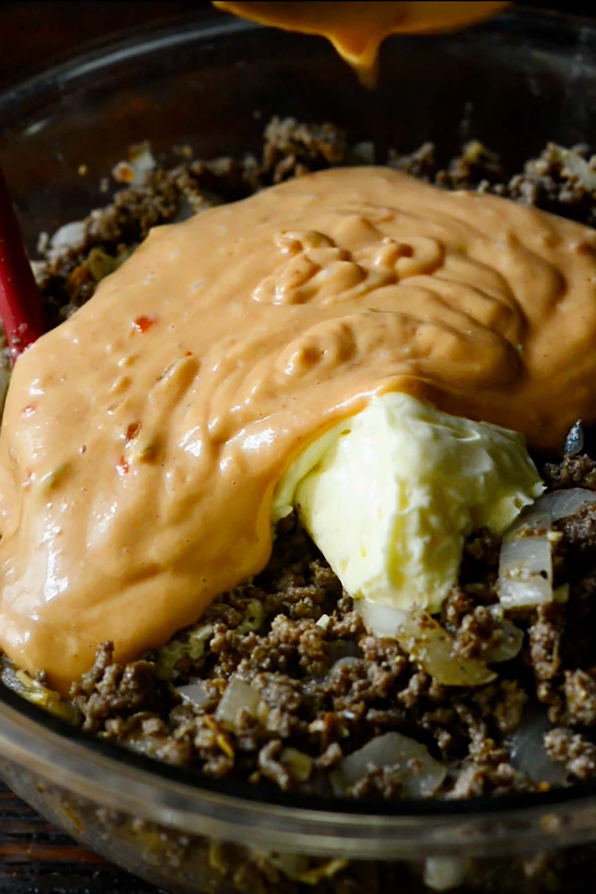 Thousand Island Dressing and Mayonnaise being stirred into a seasoned ground beef and onion mixture.