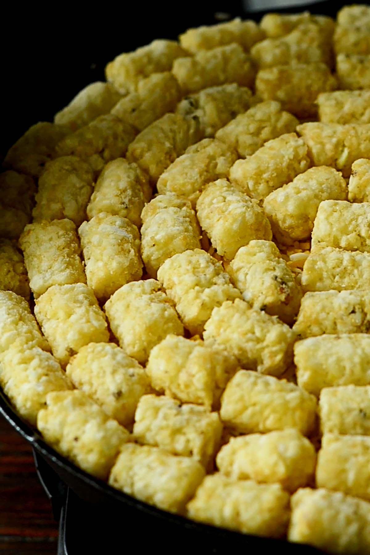 Tater tots placed over a taco tater tot casserole in a cast iron skillet.