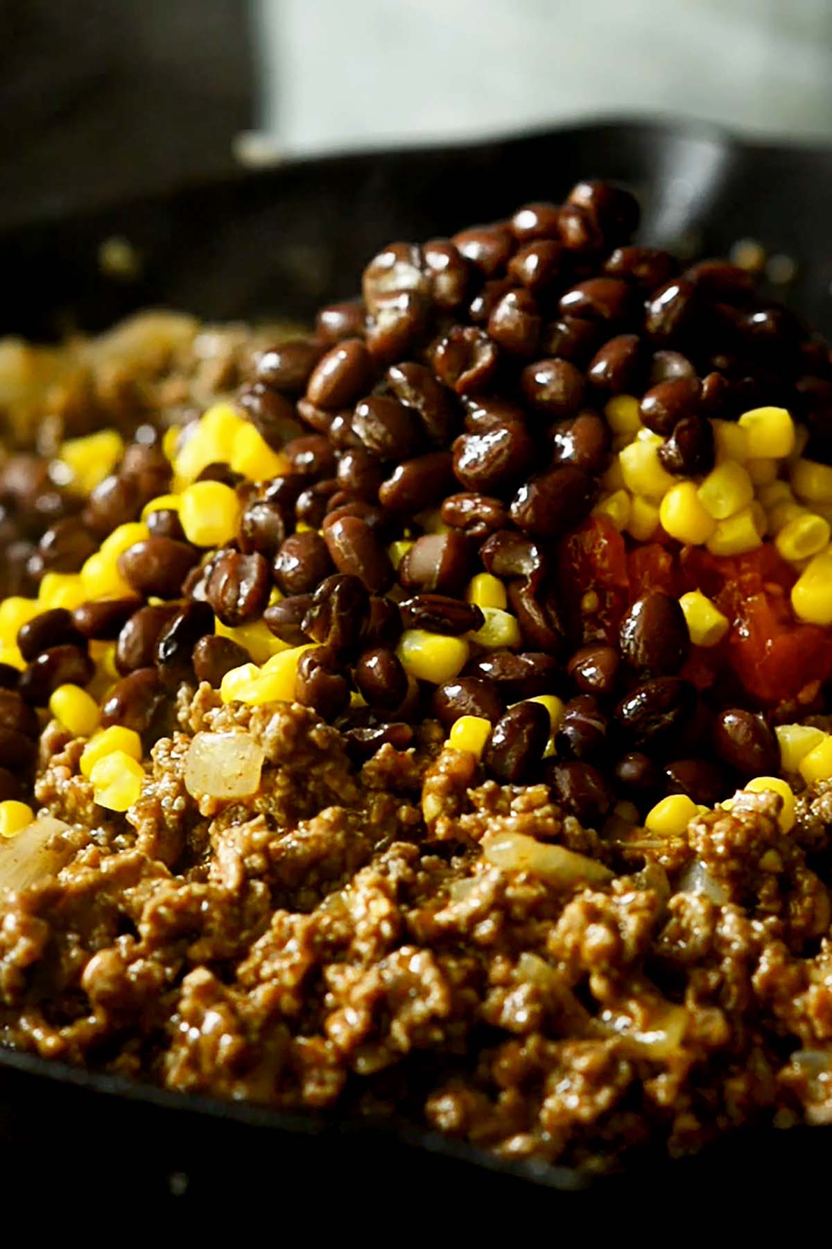 Taco seasoned ground beef in a cast iron skillet with corn, Rotel, and black beans piled on top.