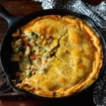 Chicken Pot Pie with cream of chicken soup served in a cast iron skillet with a slice removed revealing the creamy chicken and vegetable mixture on the inside.