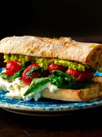 A burrata sandwich with fresh herbs, tomatoes, avocado, and balsamic glaze.