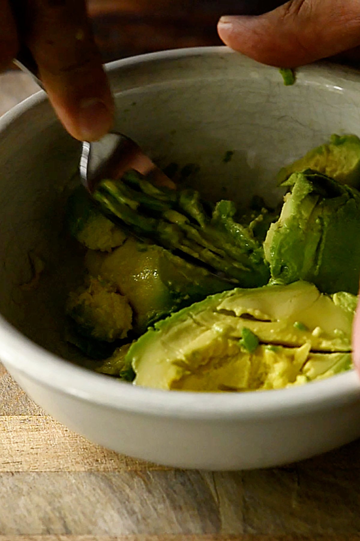 Avocado being mashed in a bowl with a fork.
