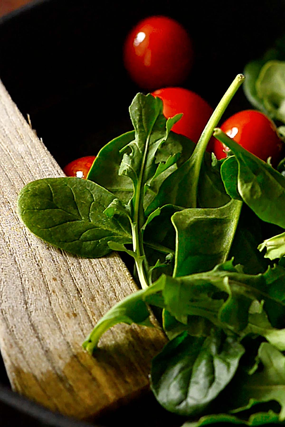 Cherry tomatoes, arugula, and spinach sautéing in a cast iron skillet.