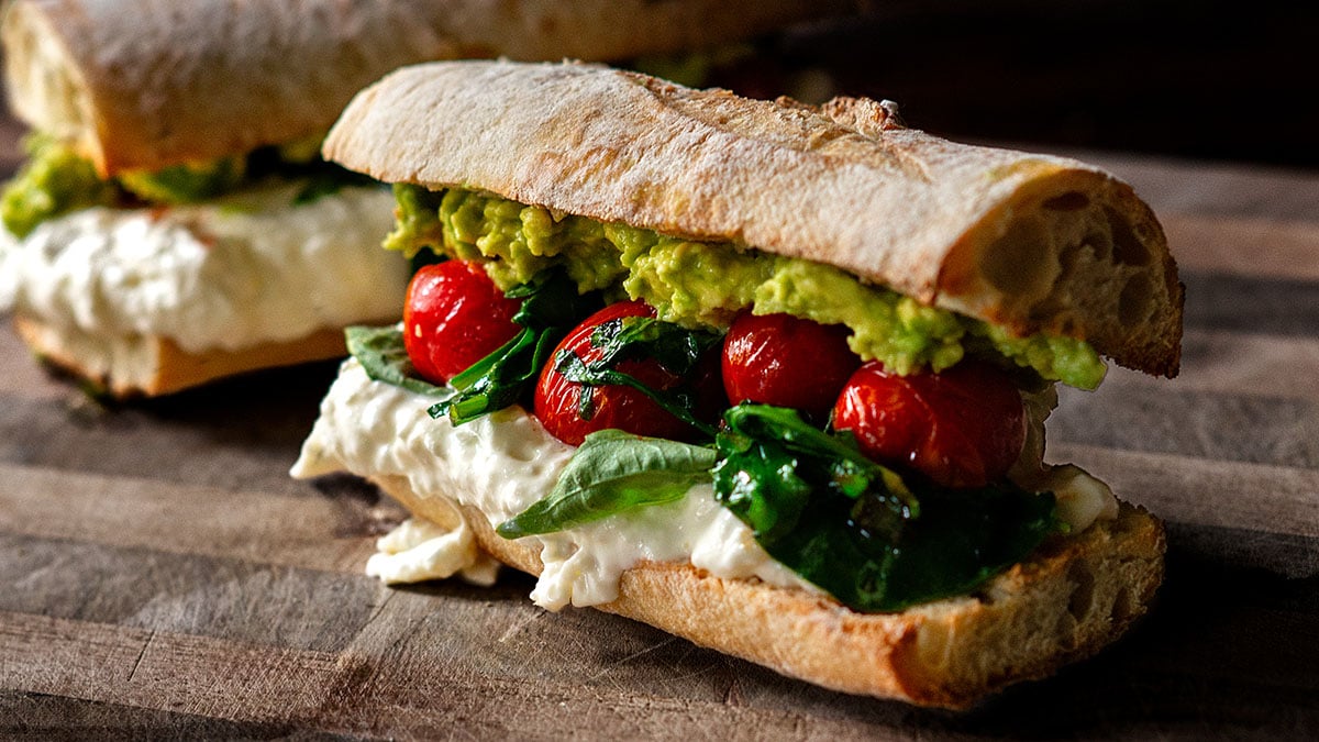 A burrata sandwich served on a wooden cutting board.