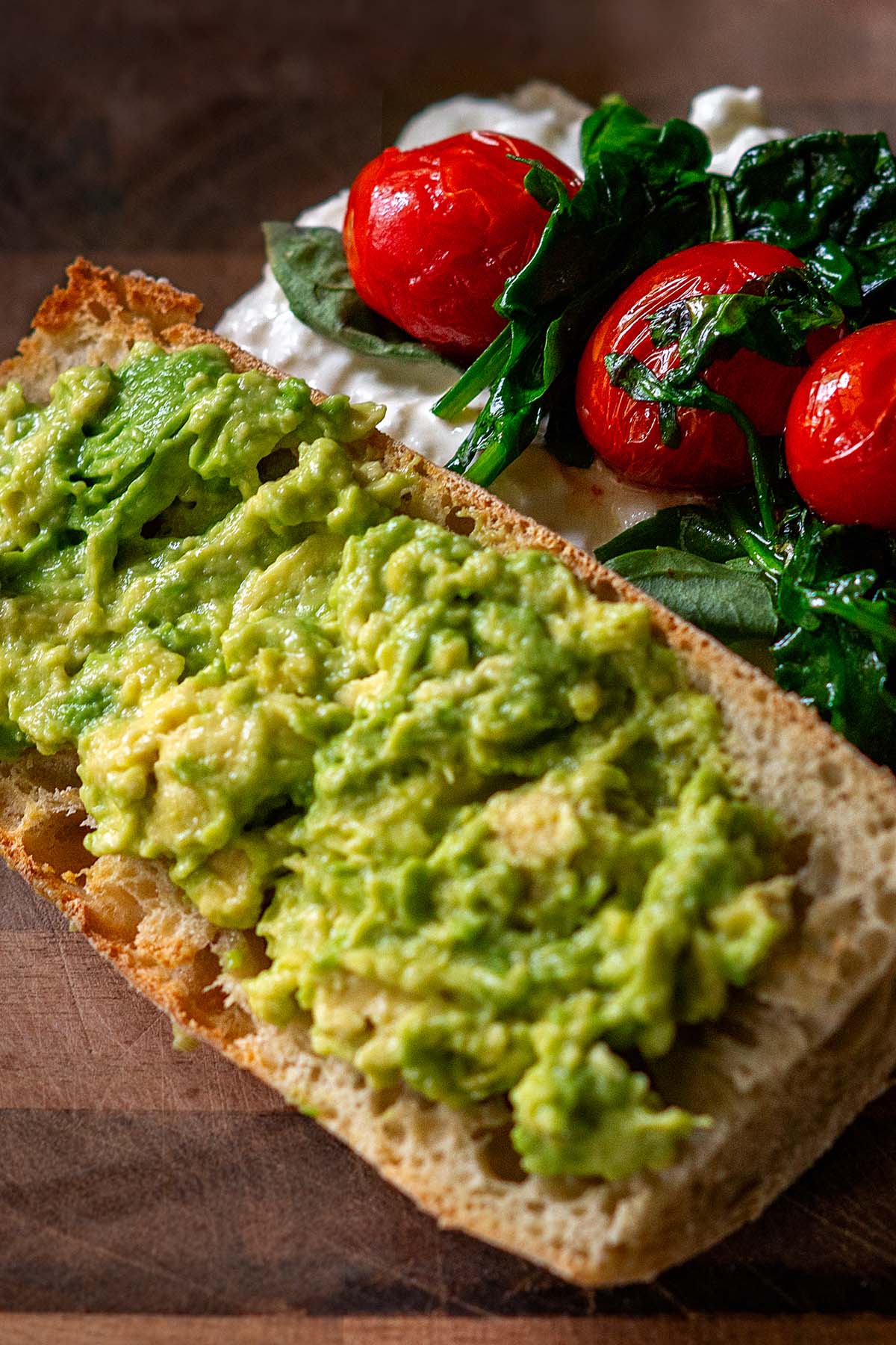 A burrata sandwich with avocado, cherry tomatoes, arugula, and spinach open faced before being assembled.