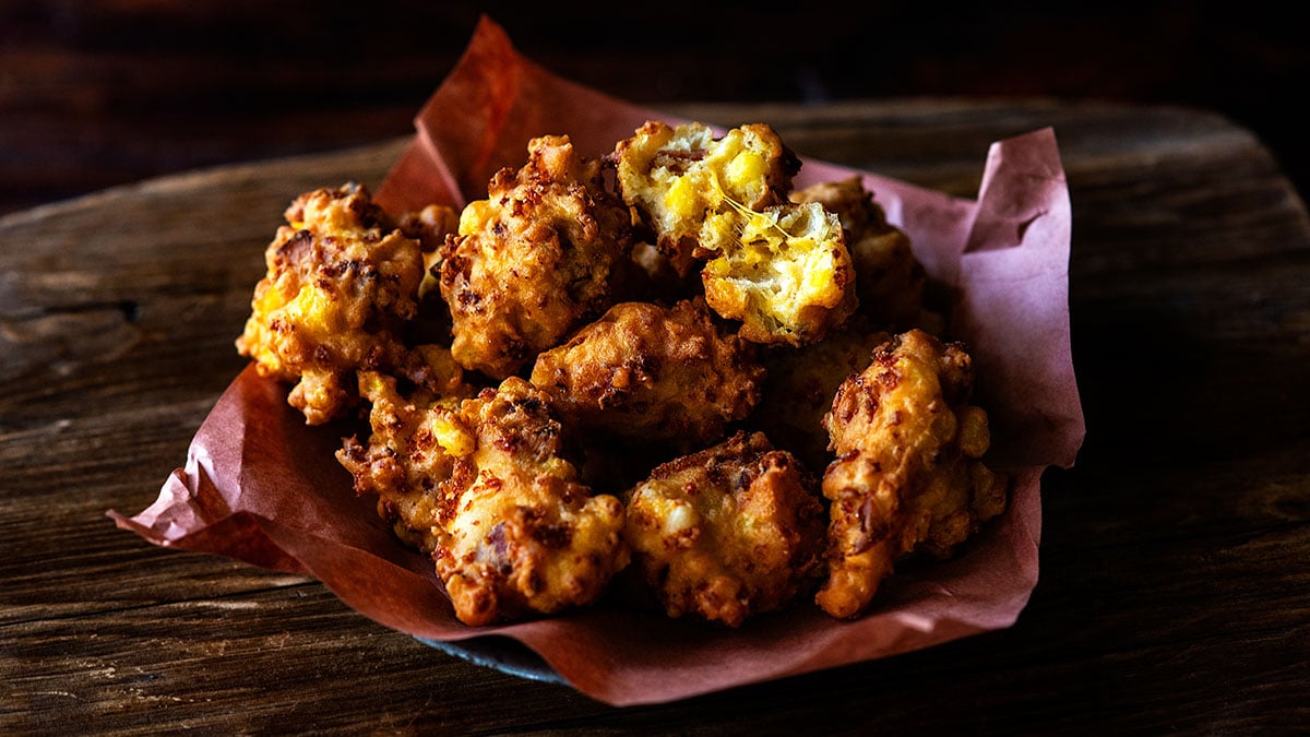 Hatch Chile Bacon Cheddar Hominy Fritters served with one sliced in half showing the inside and melted cheese.
