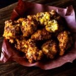 Close up of hominy fritters served in a butcher paper lined basket.