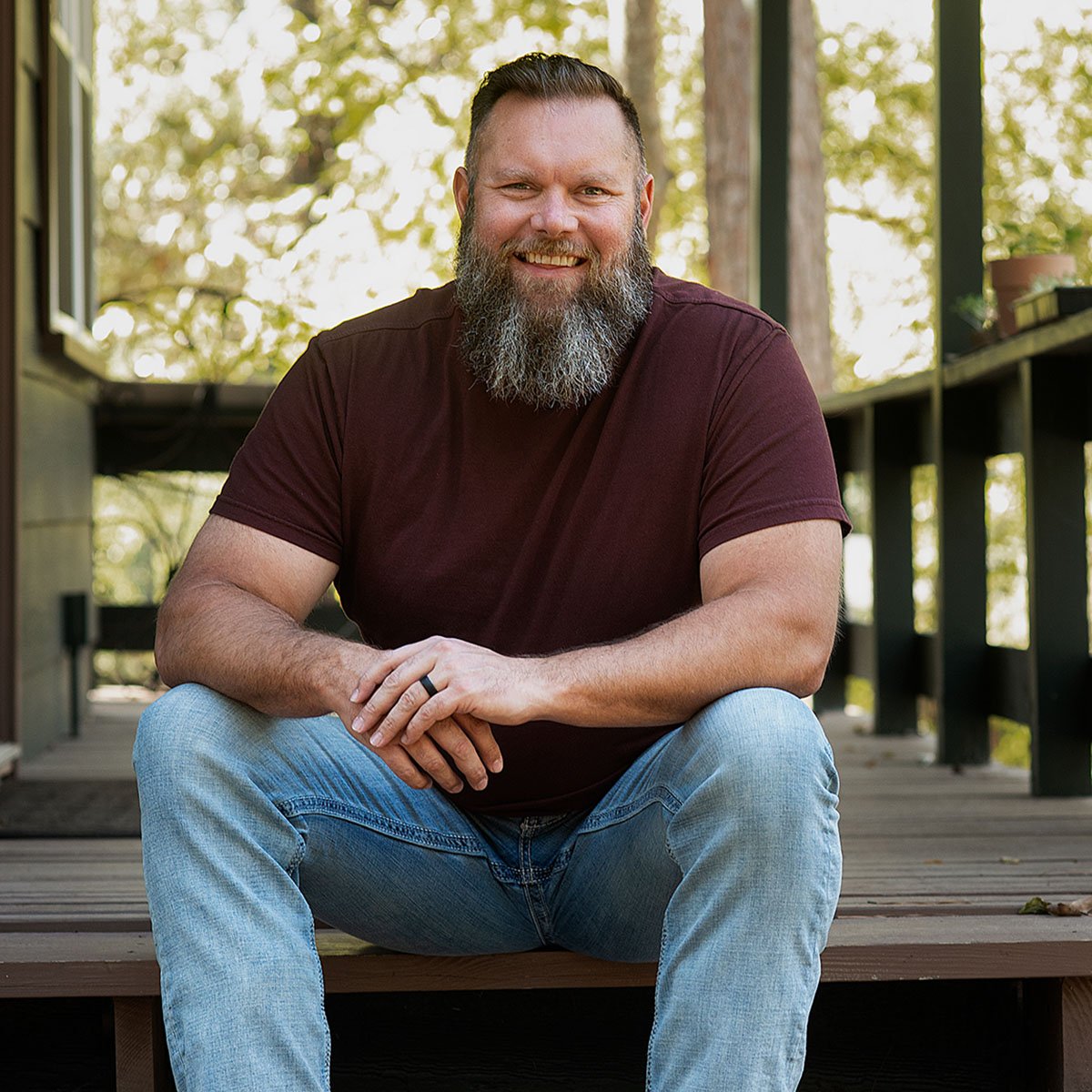 A close up photograph of Jeremy Klae sitting on the front porch of a cabin.