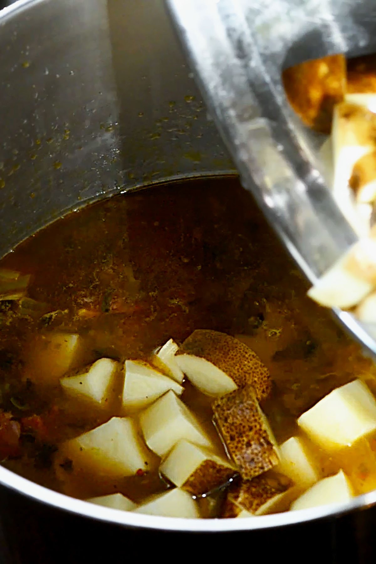 Sliced Russet Potatoes being added to a stock pot full of soup.