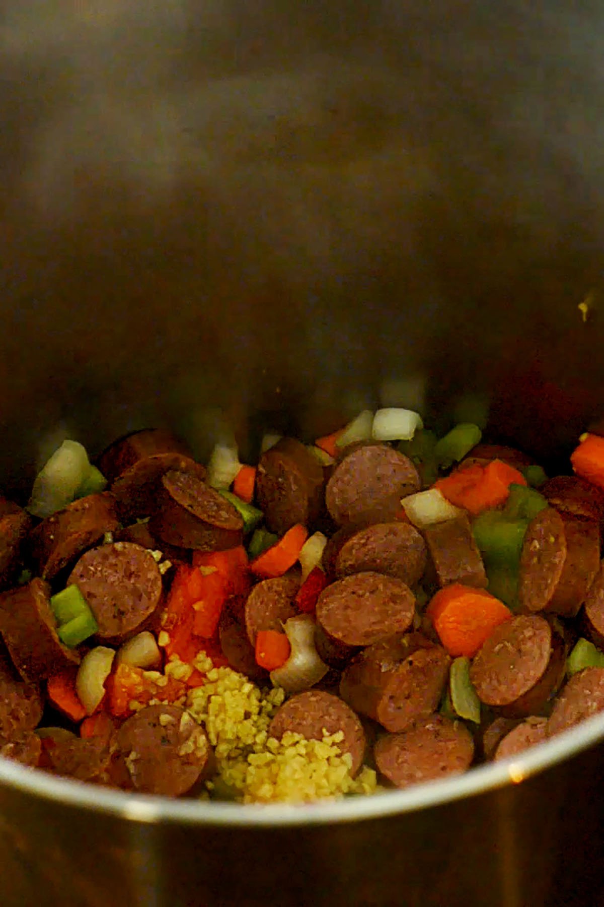 Sliced smoked sausage with sliced carrots, celery, onion, and red bell pepper sautéing in a stock pot.