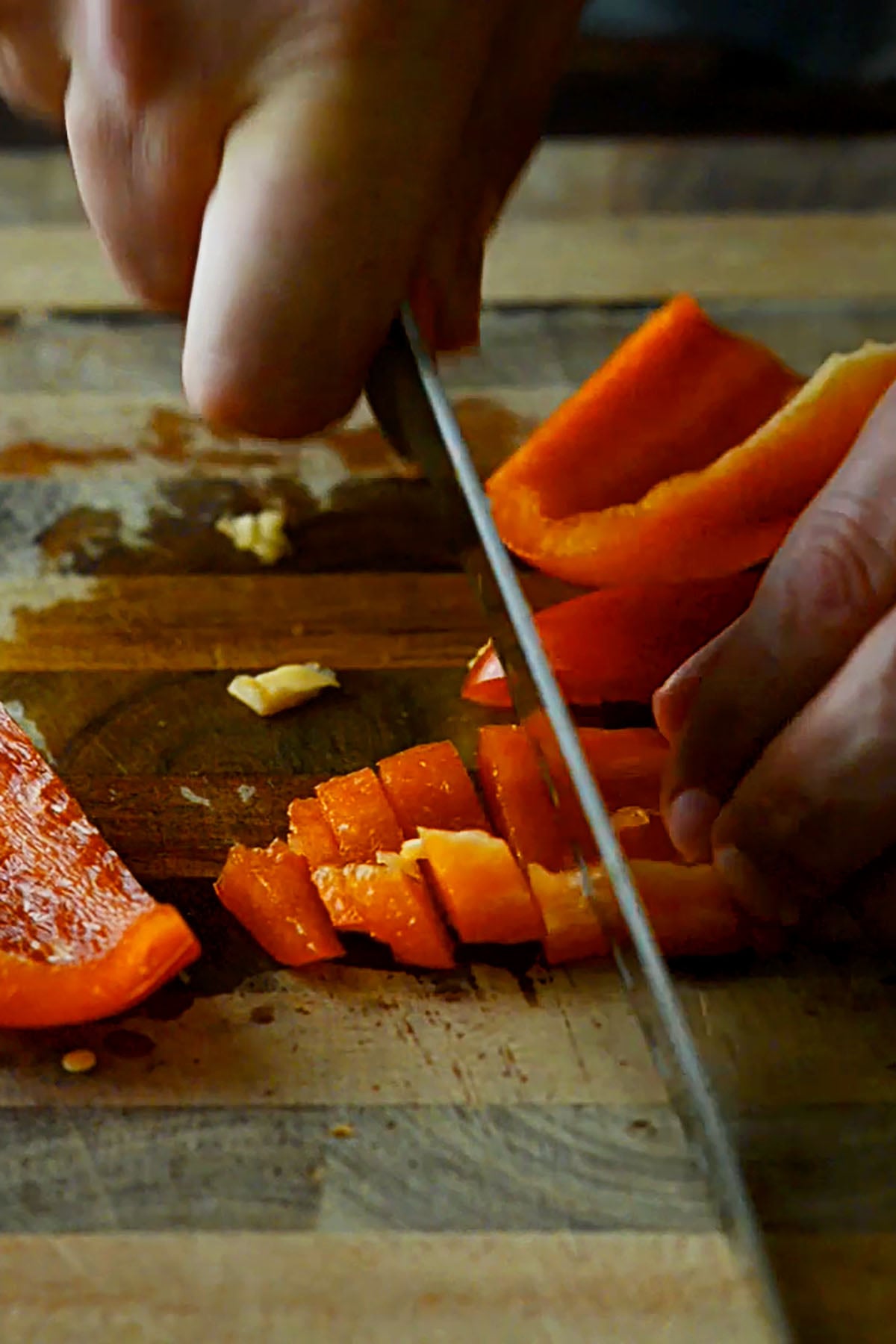 Red bell pepper being sliced on a wood cutting board.