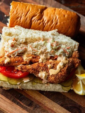 Fried Catfish Po' Boy Sandwich served with coleslaw, fresh tomato, pickles, and remoulade.