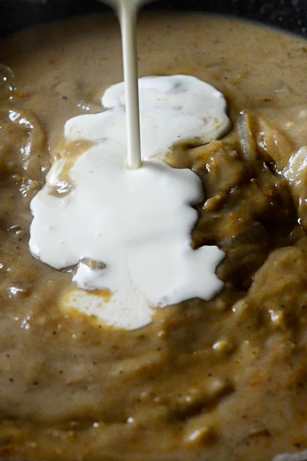 Heavy cream being poured into a thick onion gravy.