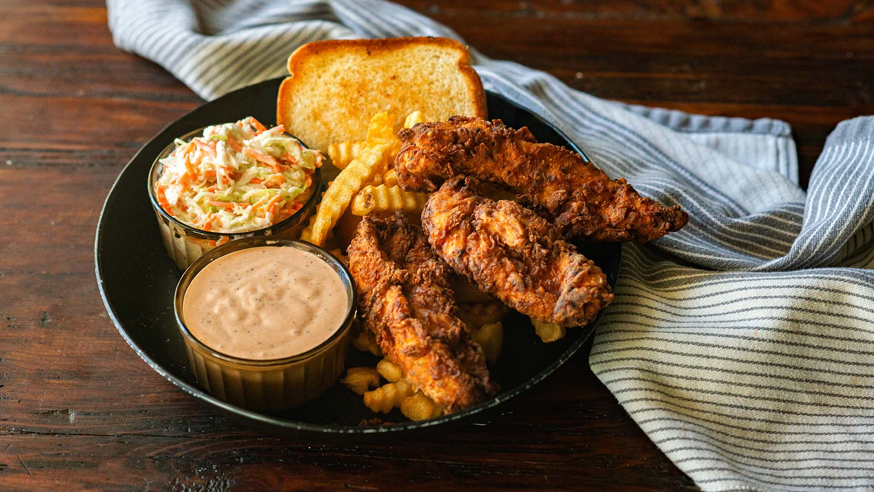 Three chicken strips, copycat cane's sauce, coleslaw and Texas toast all served in one plate.