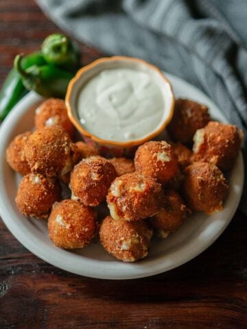 Texas Roadhouse Rattlesnake Bites served on a plate with a bowl of ranch sauce with a towel on the side and fresh jalapeños for decoration.