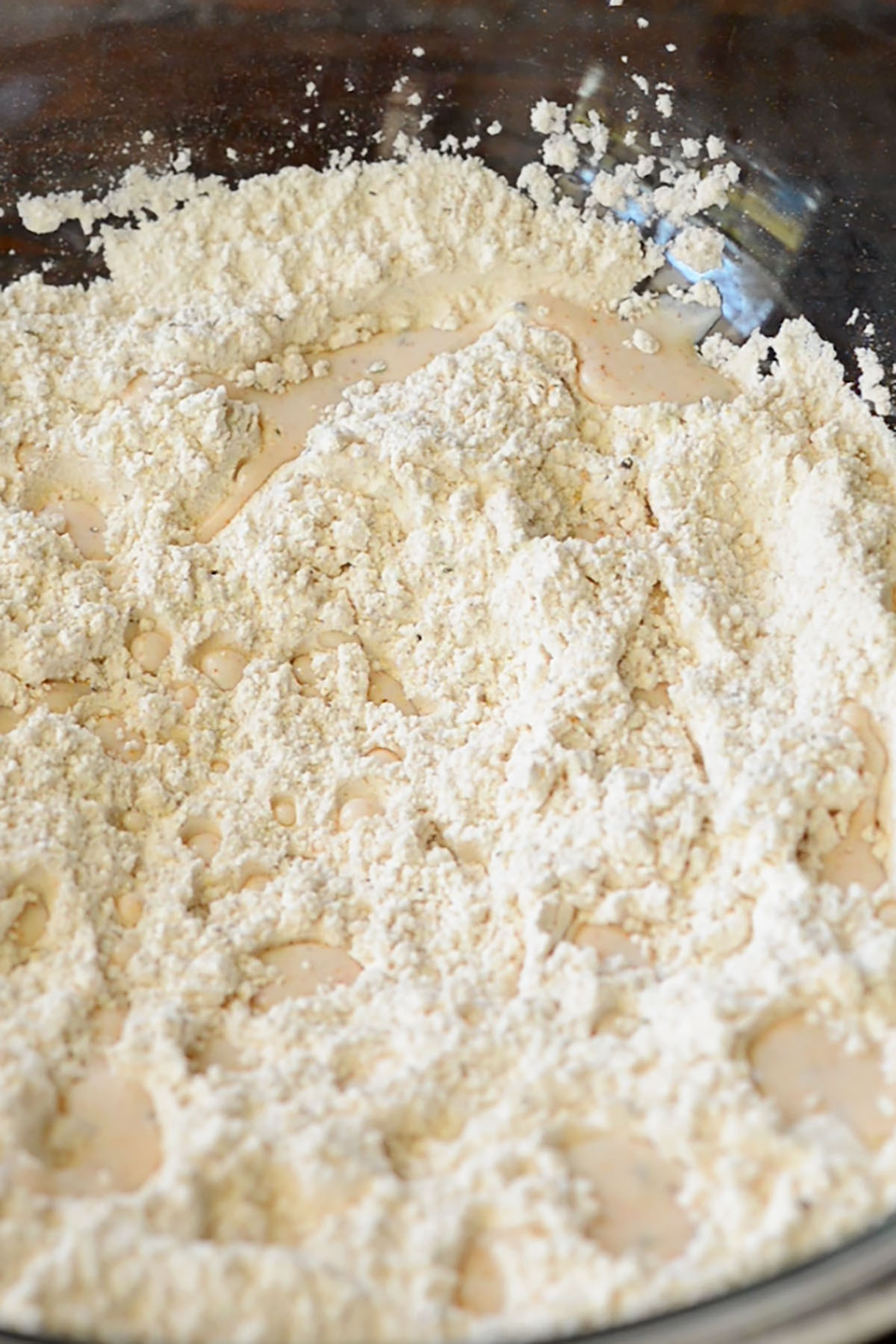 Seasoned flour in a mixing bowl with buttermilk drops for fried chicken breading.
