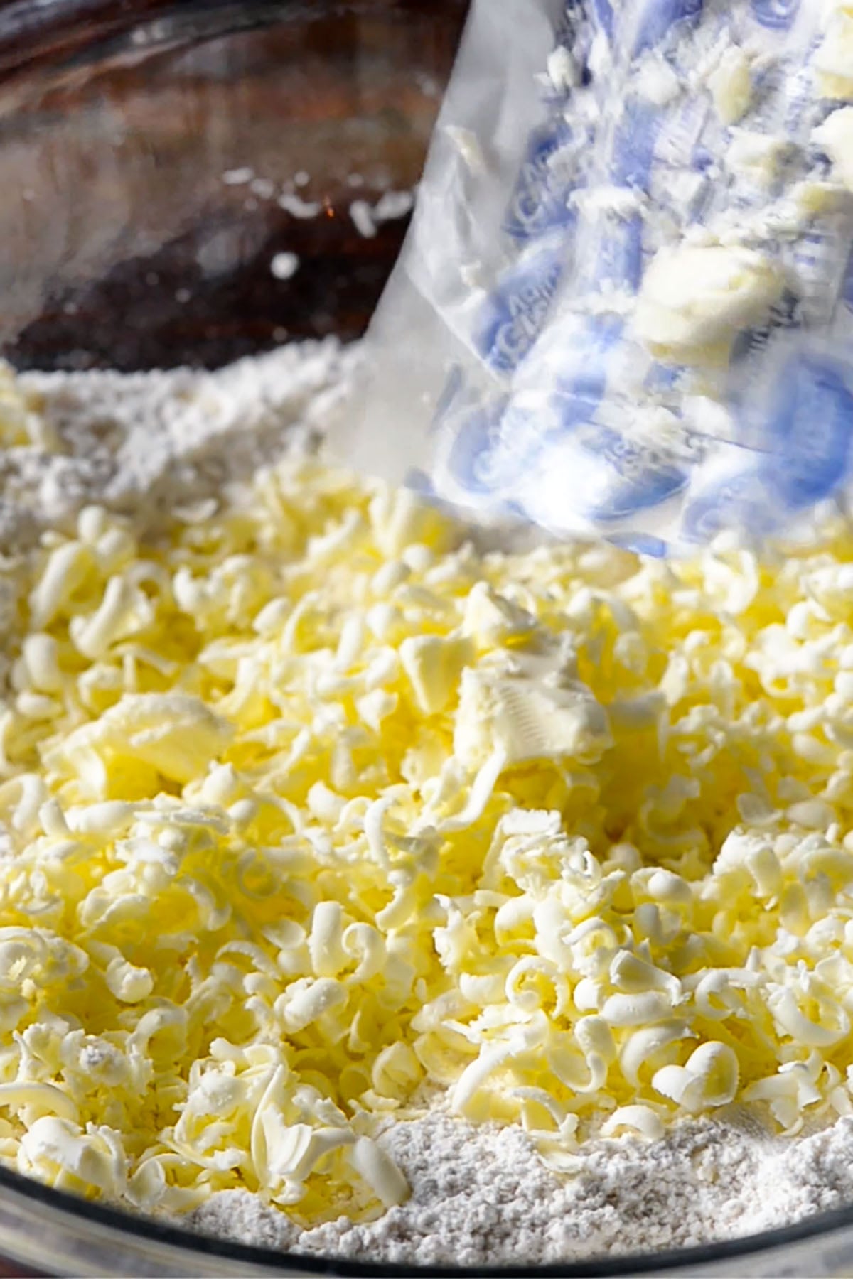 Grated frozen butter being mixed into a buttermilk biscuit flour mixture.