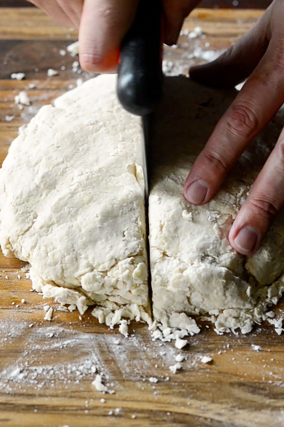 Buttermilk biscuit dough being sliced in half with a cutter to stack and form layers.