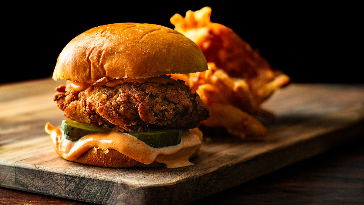 A fried chicken sandwich layered with spicy mayonnaise, sliced dill pickles, a crunchy deep fried chicken breast on a brioche bun with a serving of Cajun fries.