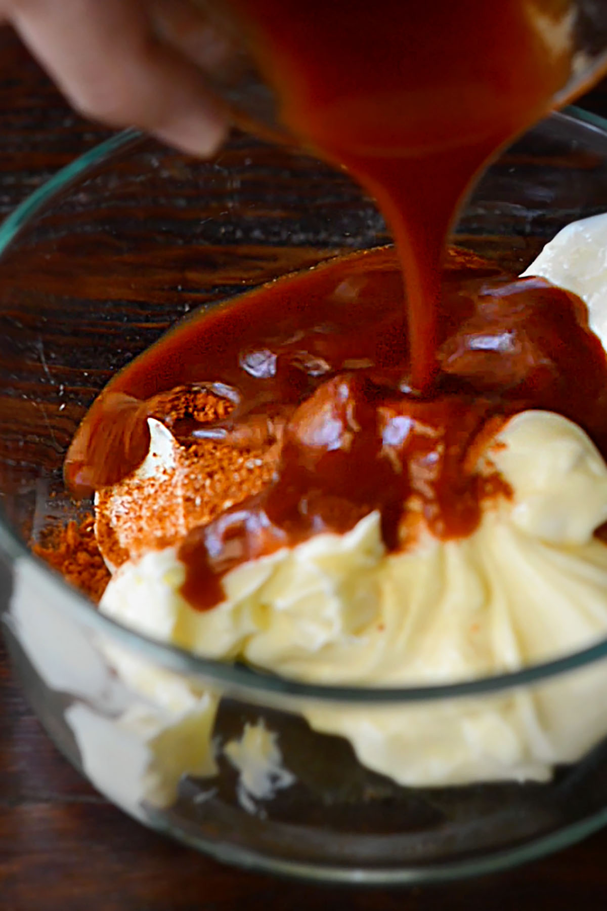 Hot sauce being poured into a bowl of mayonnaise and seasonings for spicy mayo.