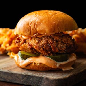 A Popeyes spicy chicken sandwich copycat served on a wood cutting board with fries in the background.