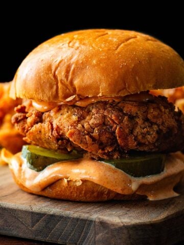 A Popeyes spicy chicken sandwich copycat served on a wood cutting board with fries in the background.