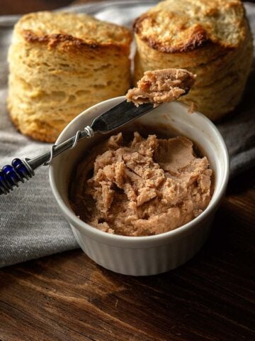 Texas Roadhouse Butter served in a small dish with a spreader full and biscuits in the background.