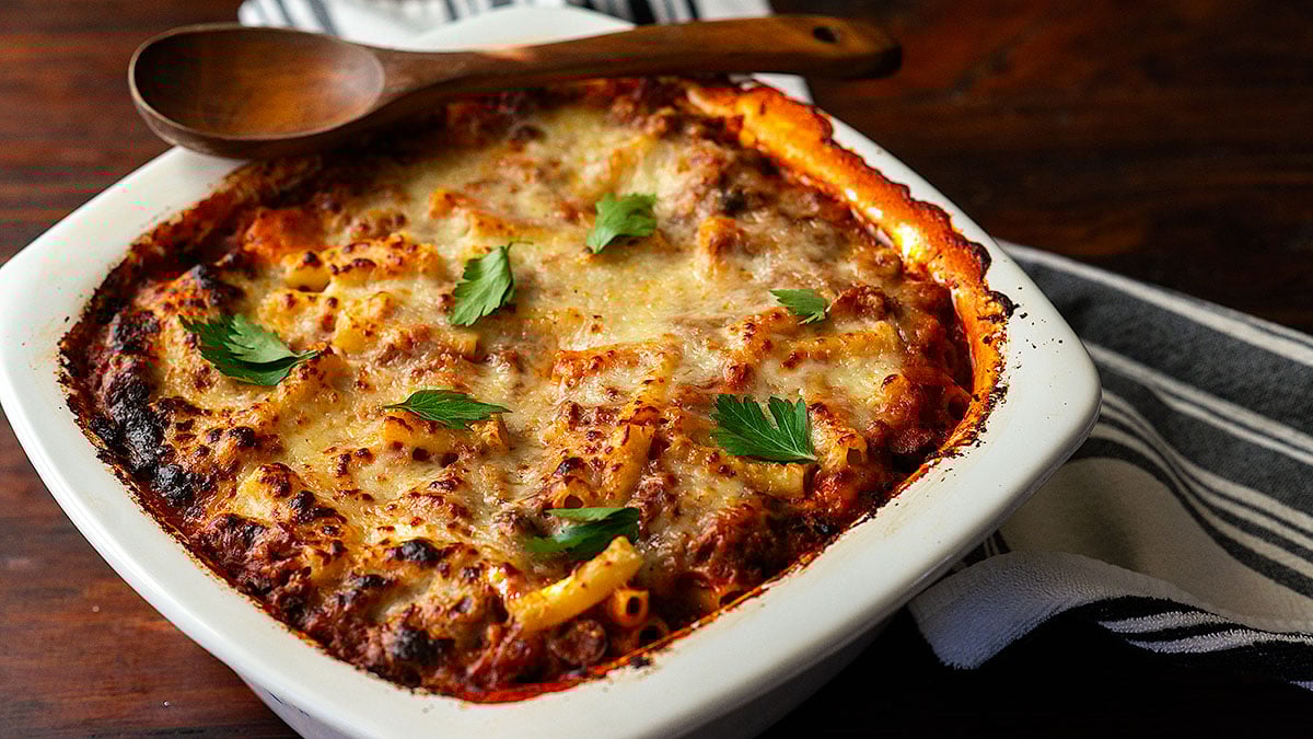 Baked Ziti with meat sauce served in a large deep baking dish topped with fresh parsley.